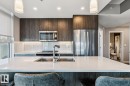 Kitchen featuring a large white countertop island with integrated sink, wood-finish cabinetry, stainless steel appliances, and subway tile backsplash - 3302 10180 103 Street, Edmonton, AB  - Indoor Photo Showing Kitchen With Double Sink With Upgraded Kitchen 