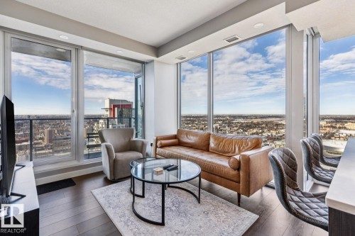 Living area featuring expansive floor-to-ceiling windows, dark wood-finish flooring, recessed ceiling lighting, and a sliding glass door opening to a balcony - 3302 10180 103 Street, Edmonton, AB - Indoor Photo Showing Living Room