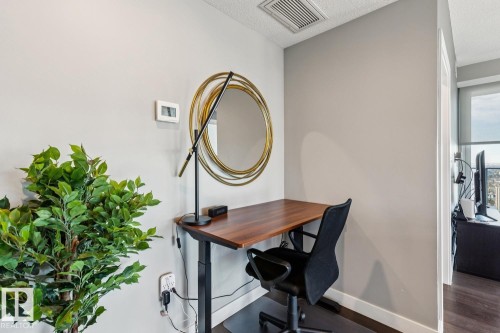 Dedicated desk space featuring a dark wood-finish desk, a modern circular mirror with a gold-tone frame, and light gray wall paint - 3302 10180 103 Street, Edmonton, AB - Indoor