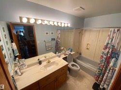 Bathroom featuring a single vanity with an integrated sink, a large wall-mounted mirror, and a full-size bathtub with an overhead shower - 