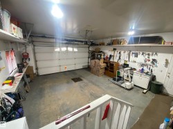 Attached garage featuring a concrete floor, white garage door with upper window inserts, overhead lighting, and built-in wall shelving - 