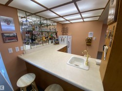 Built-in bar featuring a white countertop with an integrated sink and brass-finish faucet, mirrored shelving, and overhead fluorescent lighting - 