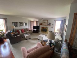 Spacious living area featuring a central fireplace with a decorative mantel and hearth, large windows, and wood-finish flooring - 