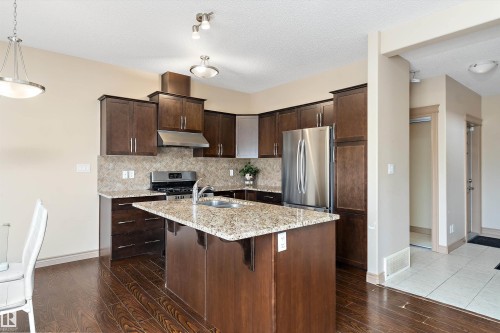 Well-appointed kitchen featuring dark wood cabinetry, stainless steel appliances, a center island with a sink, and granite countertops - 23 3103 Hilton Drive, Edmonton, AB - Indoor Photo Showing Kitchen With Double Sink With Upgraded Kitchen