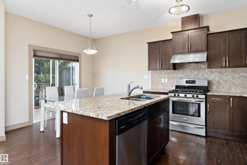 Kitchen featuring dark wood-finish cabinetry, stainless steel appliances, granite countertops, and a patterned tile backsplash - 23 3103 Hilton Drive, Edmonton, AB - Indoor Photo Showing Kitchen With Double Sink With Upgraded Kitchen