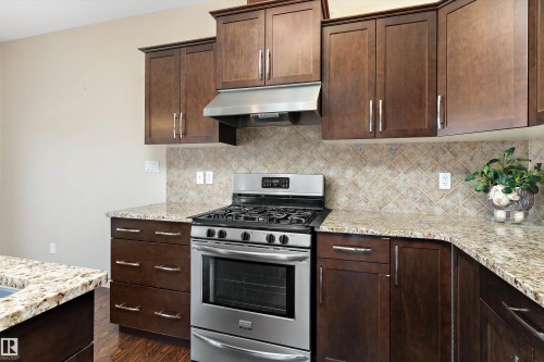 Kitchen featuring wood cabinetry, stainless steel gas range, stainless steel range hood, stone countertops, and a tiled backsplash - 23 3103 Hilton Drive, Edmonton, AB - Indoor Photo Showing Kitchen With Upgraded Kitchen