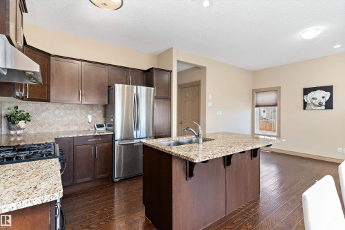 Kitchen featuring a central island with an integrated sink, granite countertops, dark wood cabinetry, stainless steel appliances, and wood-finish flooring - 23 3103 Hilton Drive, Edmonton, AB - Indoor Photo Showing Kitchen With Double Sink With Upgraded Kitchen