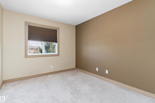 Carpeted room featuring a single window with blinds, light beige walls, and one accent wall in a deeper tan hue - 23 3103 Hilton Drive, Edmonton, AB - Indoor Photo Showing Other Room