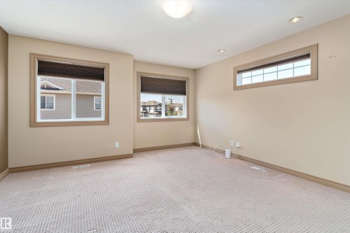 Spacious room featuring neutral carpeting, three windows with wood-trim framing, and recessed ceiling lighting - 23 3103 Hilton Drive, Edmonton, AB - Indoor Photo Showing Other Room