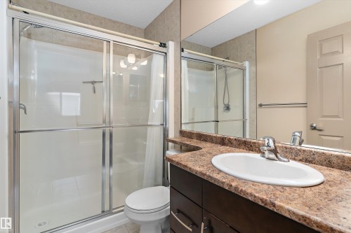 Bathroom featuring a glass-enclosed shower, dark wood-finish vanity with an oval sink, speckled countertop, and a large wall-mounted mirror - 23 3103 Hilton Drive, Edmonton, AB - Indoor Photo Showing Bathroom