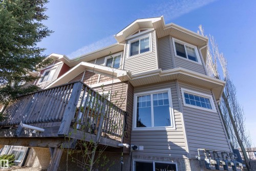 Multi-level exterior featuring light gray horizontal siding, red and brown shake siding, multiple white-framed windows, and a raised wood deck - 23 3103 Hilton Drive, Edmonton, AB - Outdoor