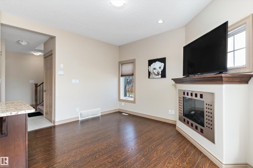 Contemporary corner fireplace with a dark wood-finish mantel, wood-finish flooring, neutral wall tones, and recessed lighting - 23 3103 Hilton Drive, Edmonton, AB - Indoor With Fireplace