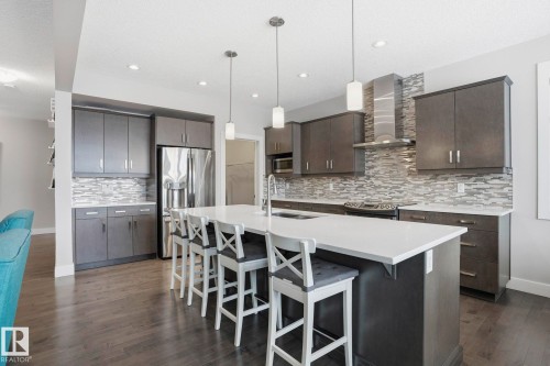 Kitchen featuring a kitchen breakfast bar, decorative light fixtures, stainless steel appliances, dark wood finish cabinets, and a kitchen island with sink - 1915 77 Street, Edmonton, AB - Indoor Photo Showing Kitchen With Upgraded Kitchen
