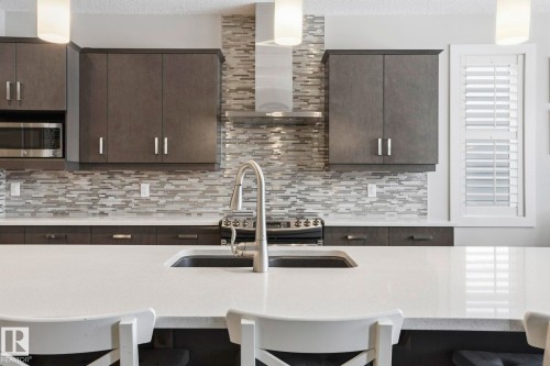 Kitchen featuring a kitchen bar, pendant lighting, light stone countertops, and a textured ceiling - 1915 77 Street, Edmonton, AB - Indoor Photo Showing Kitchen With Upgraded Kitchen