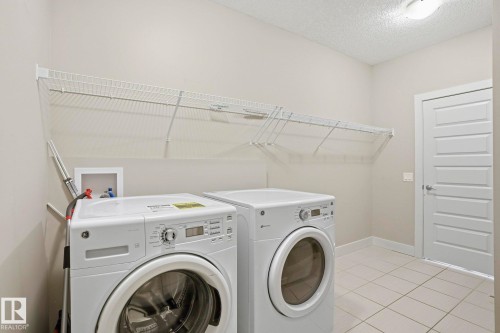 Laundry room with washing machine and dryer, a textured ceiling, and light tile patterned flooring - 1915 77 Street, Edmonton, AB - Indoor Photo Showing Laundry Room