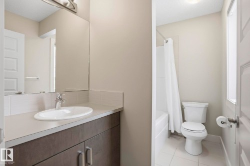 Full bath featuring vanity, shower / bathtub combination with curtain, light tile patterned flooring, and a textured ceiling - 1915 77 Street, Edmonton, AB - Indoor Photo Showing Bathroom