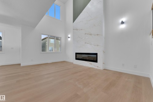 Open-concept living space featuring high ceilings, wood-finish flooring, and a contemporary fireplace with a large-format tile surround - 6226 45 Avenue, Beaumont, AB - Indoor Photo Showing Living Room With Fireplace