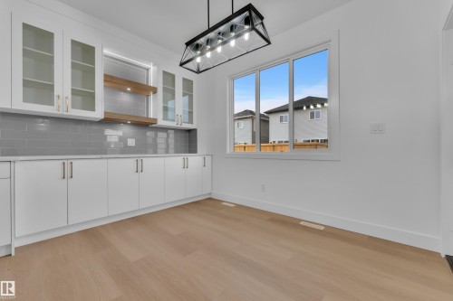 Dedicated cabinetry wall featuring white shaker-style cabinets with gold-tone hardware, a gray subway tile backsplash, and light wood open shelving with integrated lighting - 6226 45 Avenue, Beaumont, AB - Indoor Photo Showing Other Room