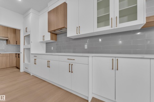 Contemporary kitchen featuring white cabinetry with gold-toned hardware, light wood-finish flooring, and a gray subway tile backsplash - 6226 45 Avenue, Beaumont, AB - Indoor Photo Showing Kitchen