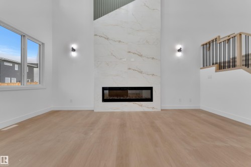 Great room featuring a full-height fireplace with large format marble-look tile, an integrated linear electric fireplace, and two wall-mounted sconces - 6226 45 Avenue, Beaumont, AB - Indoor Photo Showing Living Room With Fireplace