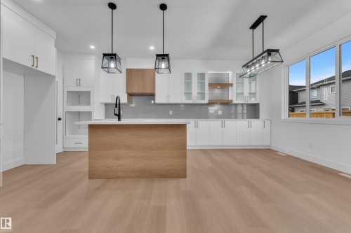 Modern kitchen featuring a wood-finish island with a white countertop, white cabinetry with gold-tone hardware, and wood-finish accent shelving - 6226 45 Avenue, Beaumont, AB - Indoor Photo Showing Kitchen