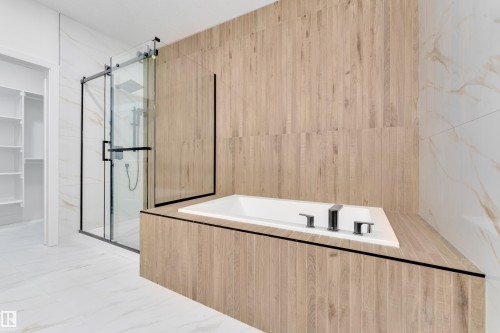 Modern bathroom featuring a built-in soaking tub with chrome fixtures, a glass-enclosed shower with a rainfall showerhead, and wood-finish wall paneling - 6226 45 Avenue, Beaumont, AB - Indoor Photo Showing Bathroom