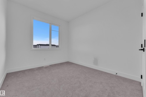 Bright room featuring a large window, neutral carpet flooring, white walls, white baseboards, and a black hardware door - 6226 45 Avenue, Beaumont, AB - Indoor Photo Showing Other Room