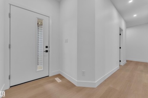 Entryway featuring a contemporary white door with a vertical glass insert, matte black hardware, light wood-finish flooring, recessed ceiling lighting, and crisp white baseboards - 6226 45 Avenue, Beaumont, AB - Indoor Photo Showing Other Room