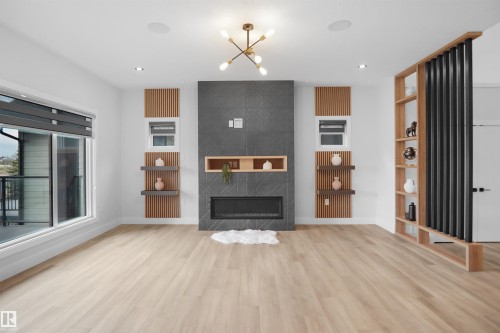 Contemporary living space featuring a tiled fireplace with built-in shelving, large windows, light wood-finish flooring, and a decorative room divider with integrated shelving - 162 Edgewater Circle, Leduc, AB - Indoor Photo Showing Living Room With Fireplace