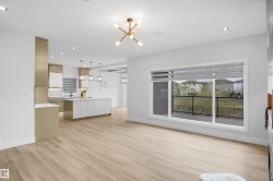 Open-concept living area with light wood-finish flooring, recessed lighting, and a contemporary linear chandelier - 
