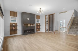 Spacious living area featuring light wood-finish flooring, a contemporary fireplace with dark tile surround and integrated shelving, and a modern chandelier - 