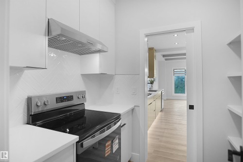 Modern kitchen featuring a stainless steel range with a flat cooktop, a coordinating range hood, white flat-panel cabinetry, white solid surface countertops, and a white herringbone tile backsplash - 162 Edgewater Circle, Leduc, AB - Indoor Photo Showing Kitchen