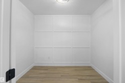 Neutral interior space featuring wood-finish flooring, a grid-pattern accent wall, white baseboards, and a flush-mount ceiling light fixture - 
