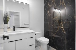Bathroom featuring a black marble-patterned accent wall, white vanity with integrated sink, black hardware, framed wall mirror, and modern lighting fixture - 