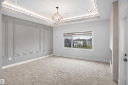 Carpeted room featuring a geometric chandelier, tray ceiling with recessed lighting, an expansive window, and a built-in fireplace - 