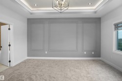 Carpeted room featuring a decorative accent wall with panel molding, a tray ceiling with recessed lighting, and a contemporary geometric chandelier - 