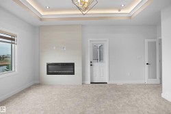 Spacious room featuring a tray ceiling with recessed lighting, a modern electric fireplace with a light-toned surround, light-colored carpeting, and a window offering a water view - 