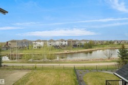 Landscaped property with a green lawn, a dark metal fence, and a paved pathway bordering a pond - 