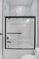 Shower/tub combination with matte black fixtures and a sliding glass enclosure - 