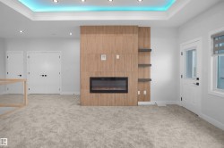 Electric fireplace with a wood-finish accent wall, integrated shelving, recessed lighting, cove lighting, and light gray carpeting - 