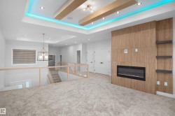 Carpeted upper-level space featuring a contemporary fireplace with a wood-finish accent wall, built-in shelving, glass panel railings, and a tray ceiling with recessed lighting - 