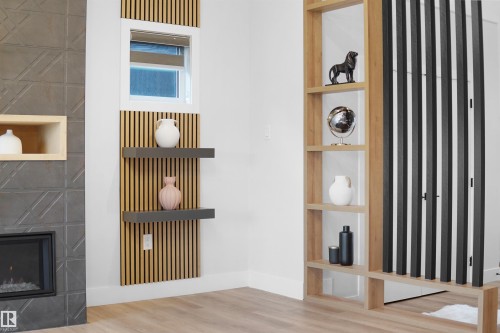 Corner architectural feature wall with light wood-finish vertical slats, a built-in window, and two floating shelves - 162 Edgewater Circle, Leduc, AB - Indoor With Fireplace