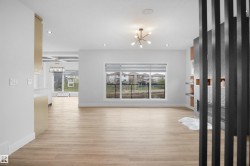 Bright open-concept living space with wood-finish flooring, a contemporary fireplace with patterned tile surround, a decorative room divider, and abundant natural light from multiple windows - 