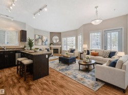 The living area features wood-look flooring, a kitchen island with a stone countertop, and a fireplace with a stone surround - 