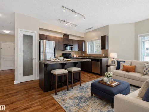 Open concept living area featuring wood-look flooring, a kitchen with dark cabinetry and stainless steel appliances, and track lighting - 120 8931 156 Street, Edmonton, AB - Indoor