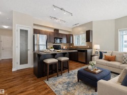 Open concept living area featuring wood-look flooring, a kitchen with dark cabinetry and stainless steel appliances, and track lighting - 