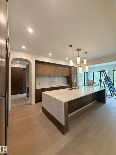 Kitchen featuring a waterfall island with a stone countertop, wood-finish cabinetry, integrated sink, and pendant lighting - 14702 Park Drive, Edmonton, AB - Indoor Photo Showing Kitchen