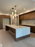 Spacious kitchen featuring a large waterfall island with integrated sink, wood-finish cabinetry, light wood-finish flooring, recessed lighting, and elegant pendant light fixtures - 14702 Park Drive, Edmonton, AB  - Indoor Photo Showing Kitchen 