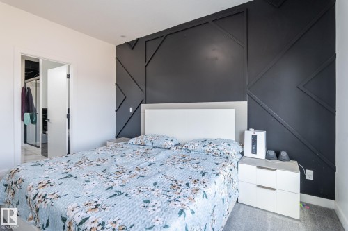 Bedroom featuring a decorative accent wall with geometric molding, white headboard, and light gray carpet flooring - 6607 50A Avenue, Beaumont, AB - Indoor Photo Showing Bedroom