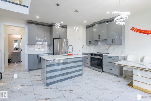 Modern kitchen featuring high-gloss gray cabinetry, stainless steel appliances, a center island with a white countertop and contrasting striped paneling, and white marble-look flooring extending throughout - 6607 50A Avenue, Beaumont, AB - Indoor Photo Showing Kitchen With Upgraded Kitchen